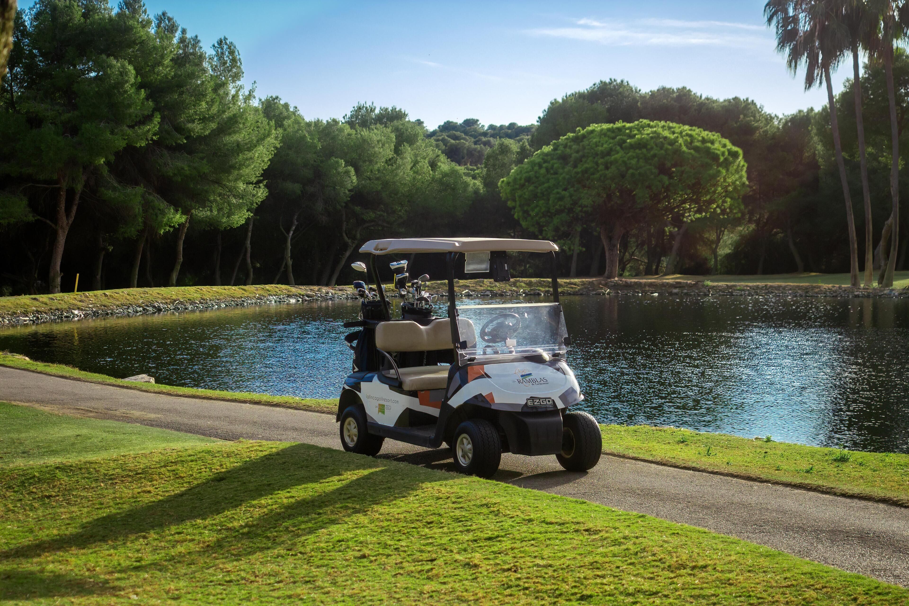 A golf cart on a paved path beside a body of water, surrounded by trees.