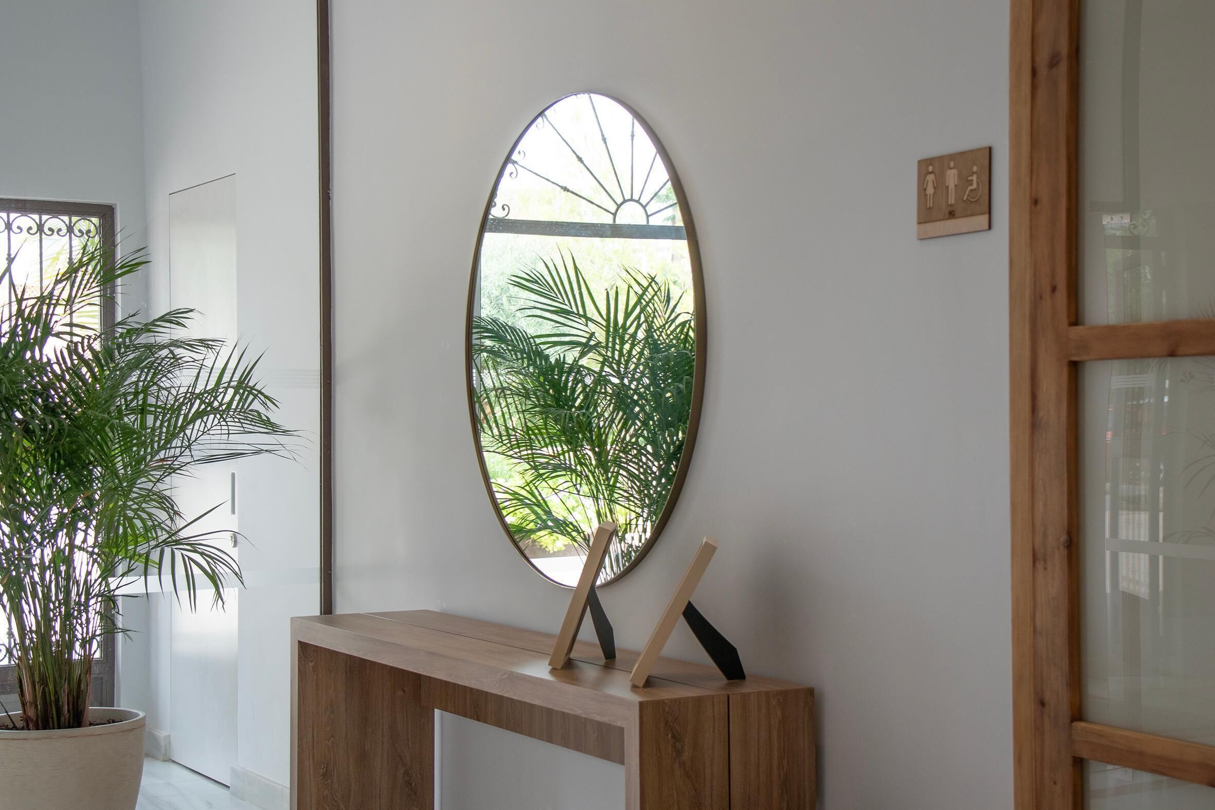 Een kamer met een houten consoletafel, een potplant en een ovaal spiegel aan de muur die groen reflecteert.