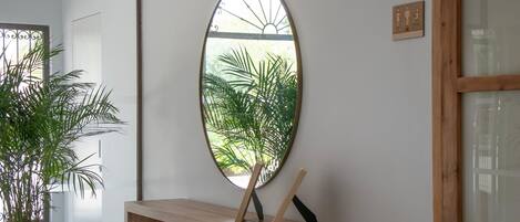 A room with a wooden console table, a potted plant, and a wall-mounted oval mirror reflecting greenery.