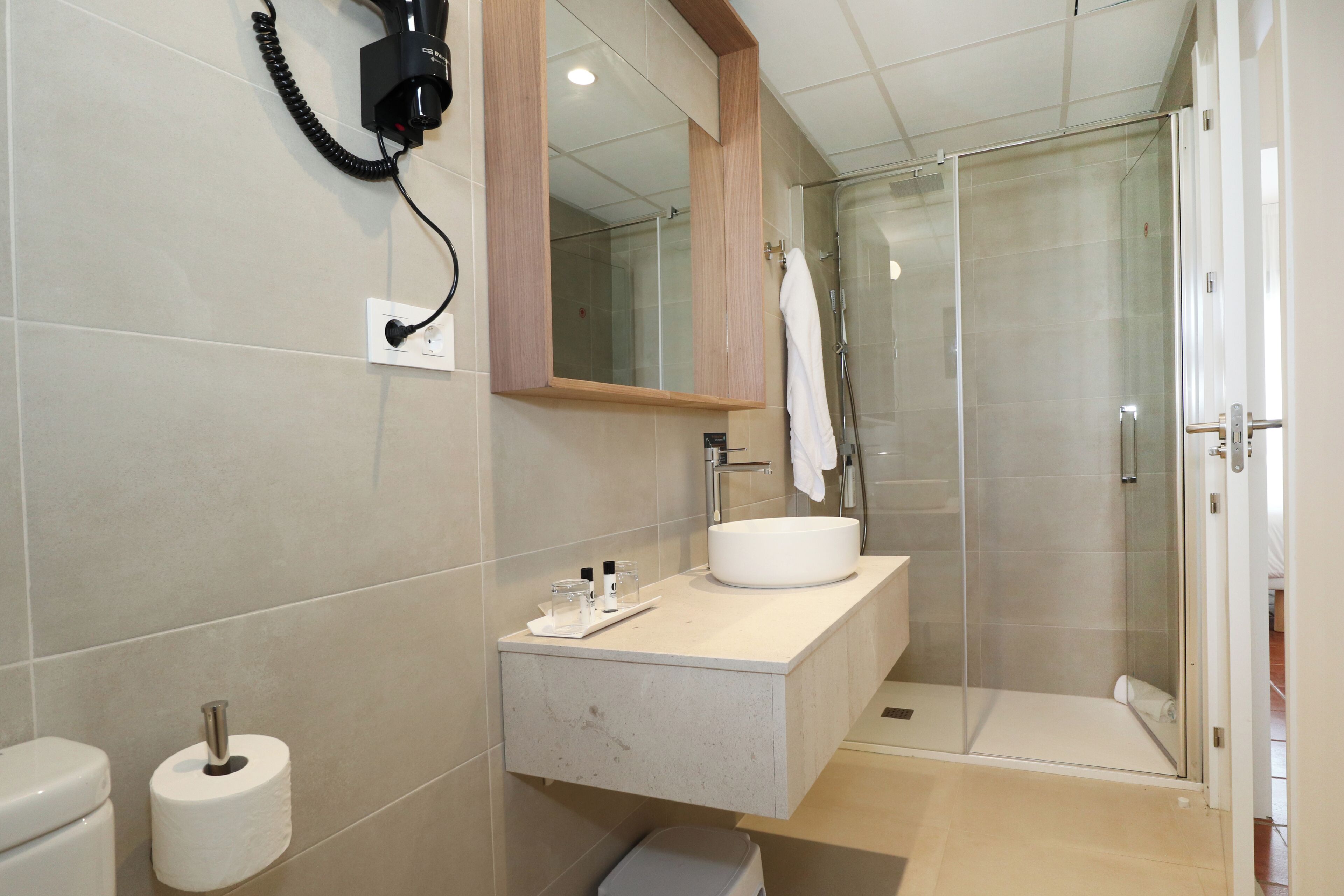 A modern bathroom with a toilet, a sink, a mirror, a shower, and a telephone mounted on the wall.