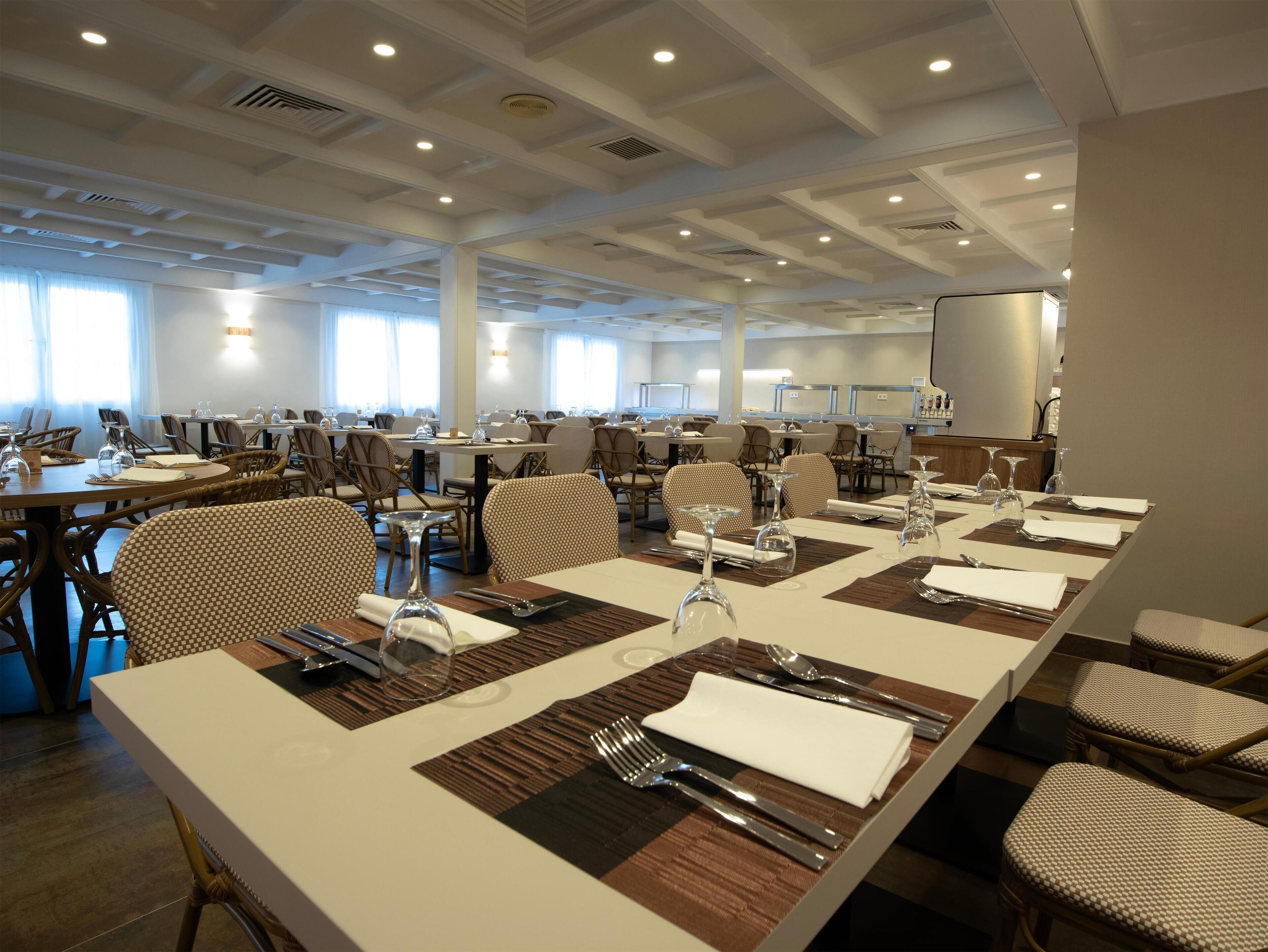 A spacious dining area with multiple tables set for meals, featuring a mix of wicker and upholstered chairs.