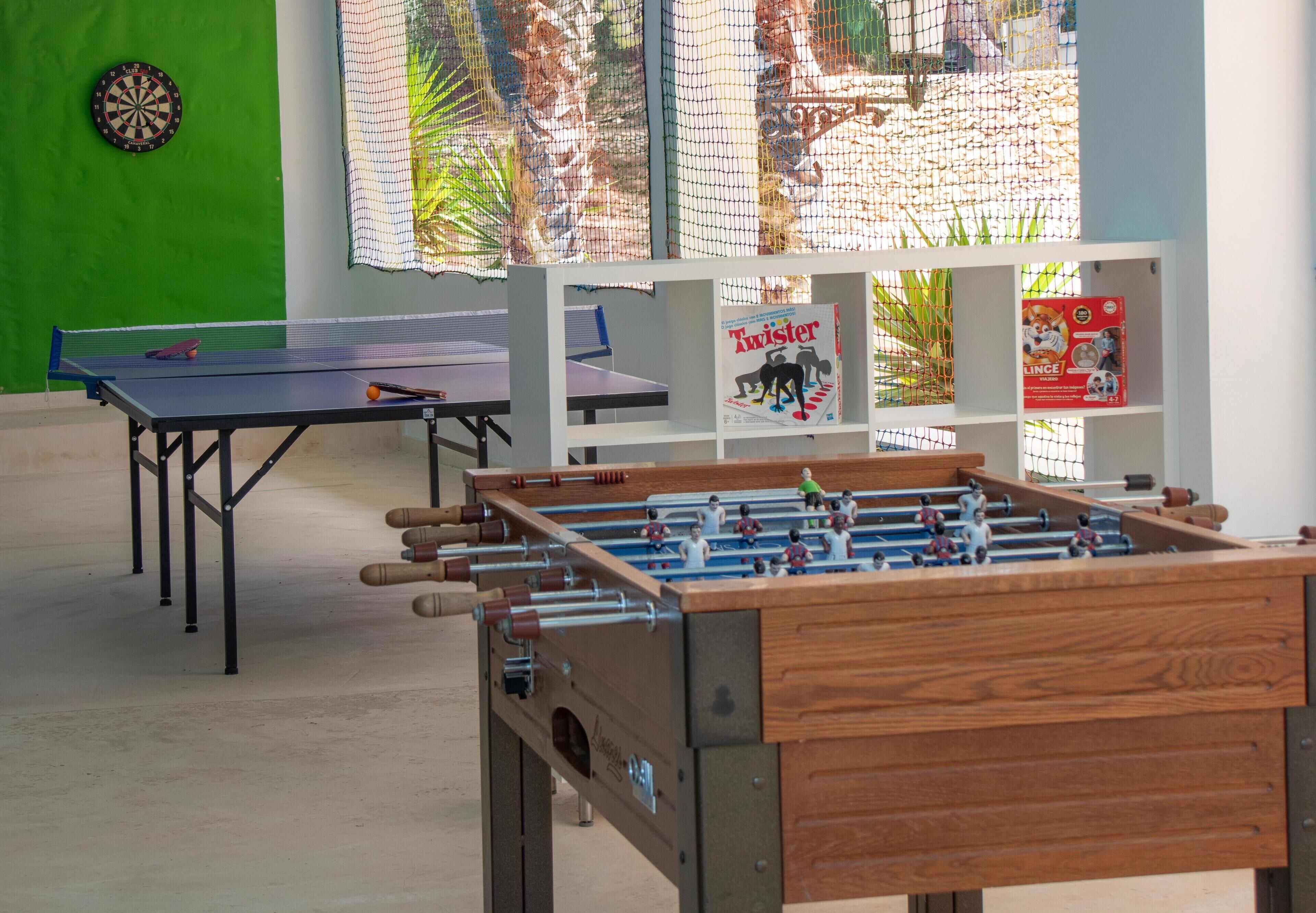 Une pièce équipée d’un baby-foot, d’une table de ping-pong et d’un jeu de fléchettes. On y trouve également des étagères remplies de magazines et une fenêtre donnant sur des palmiers.