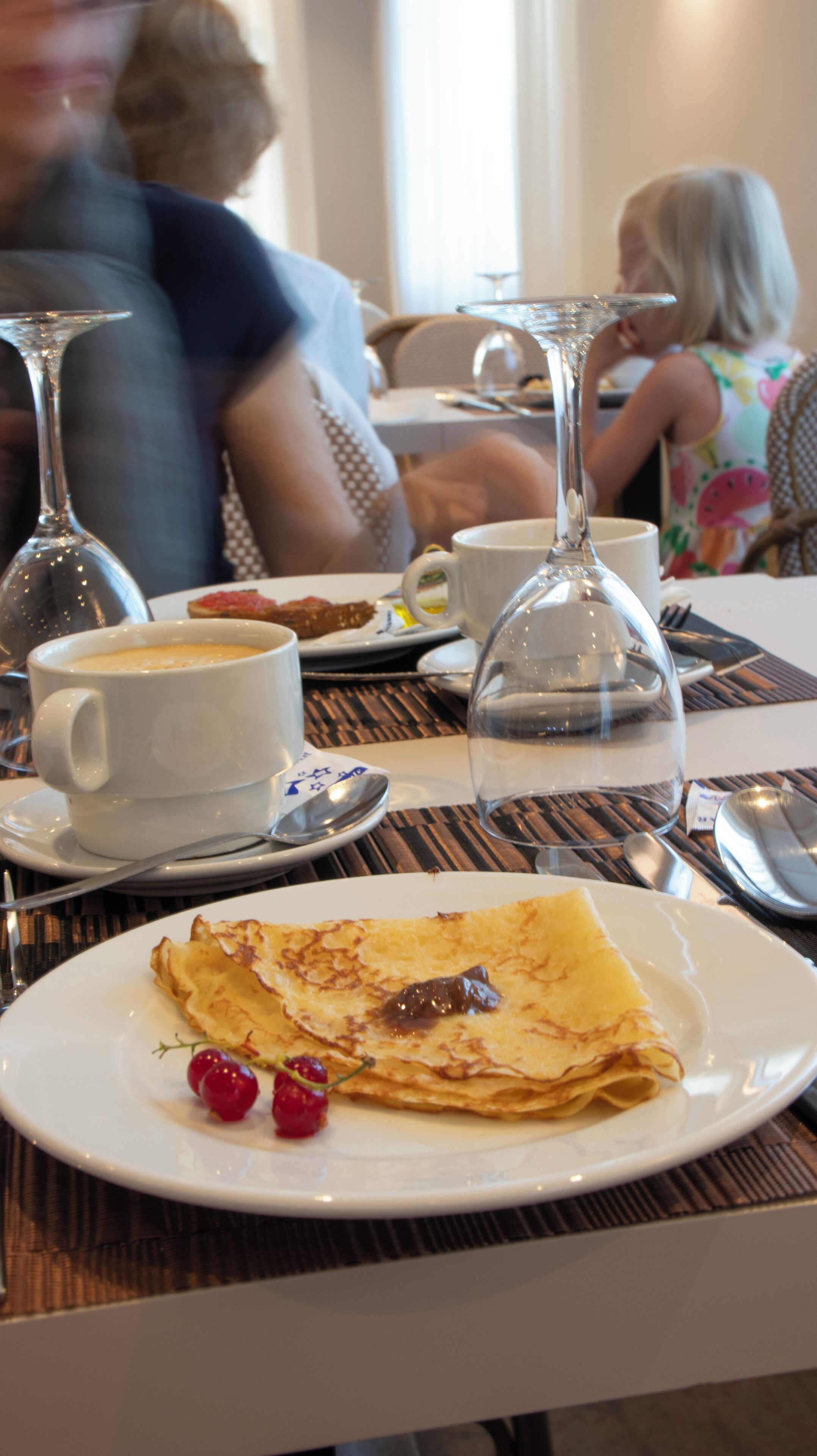 A dining table with a plate of crepes, a cup of coffee, and a wine glass.
