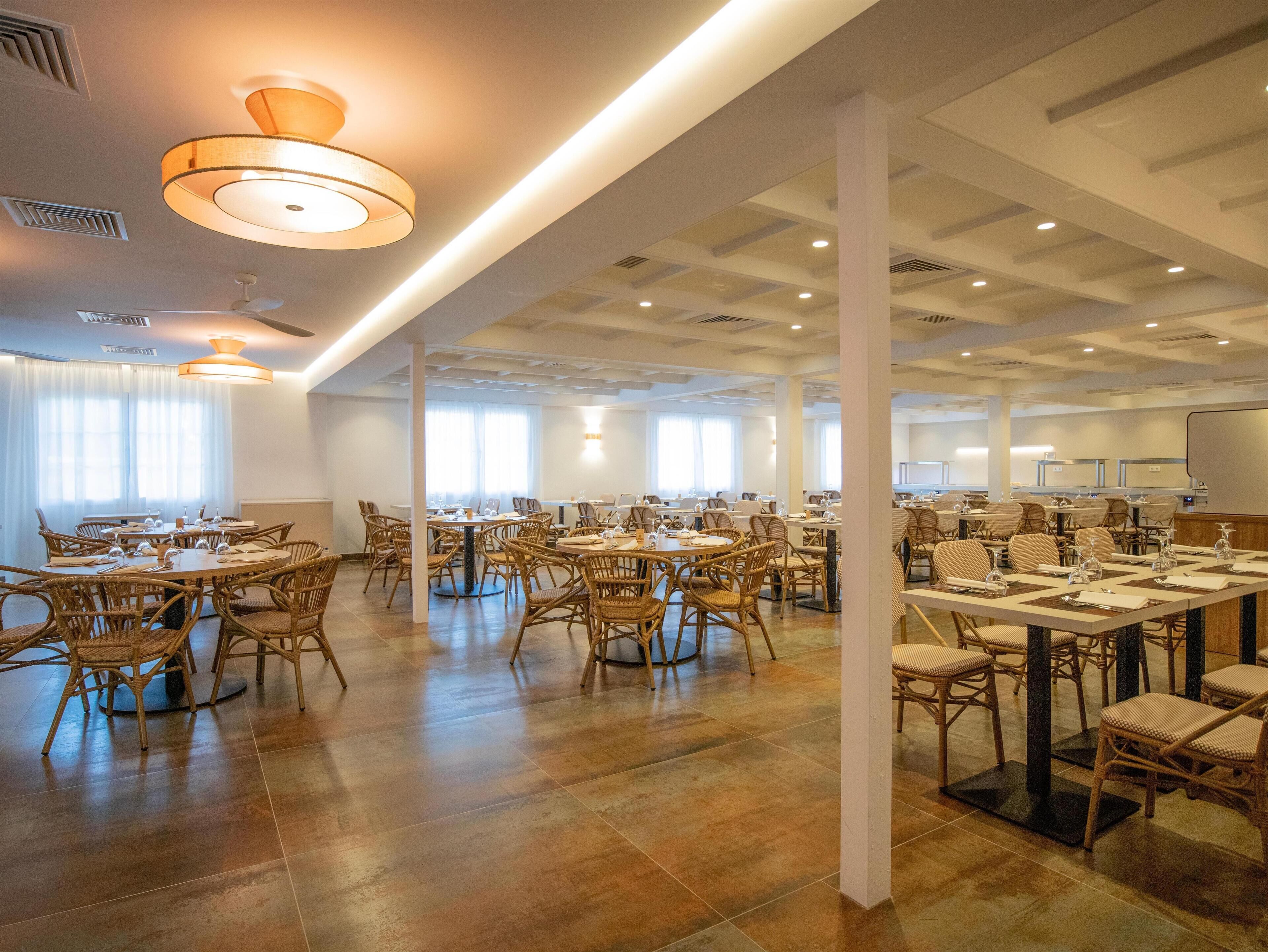 A spacious conference room with multiple tables and chairs, large windows, and modern lighting fixtures.