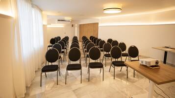 Un salón de conferencias con filas de sillas, una mesa de madera y un proyector.