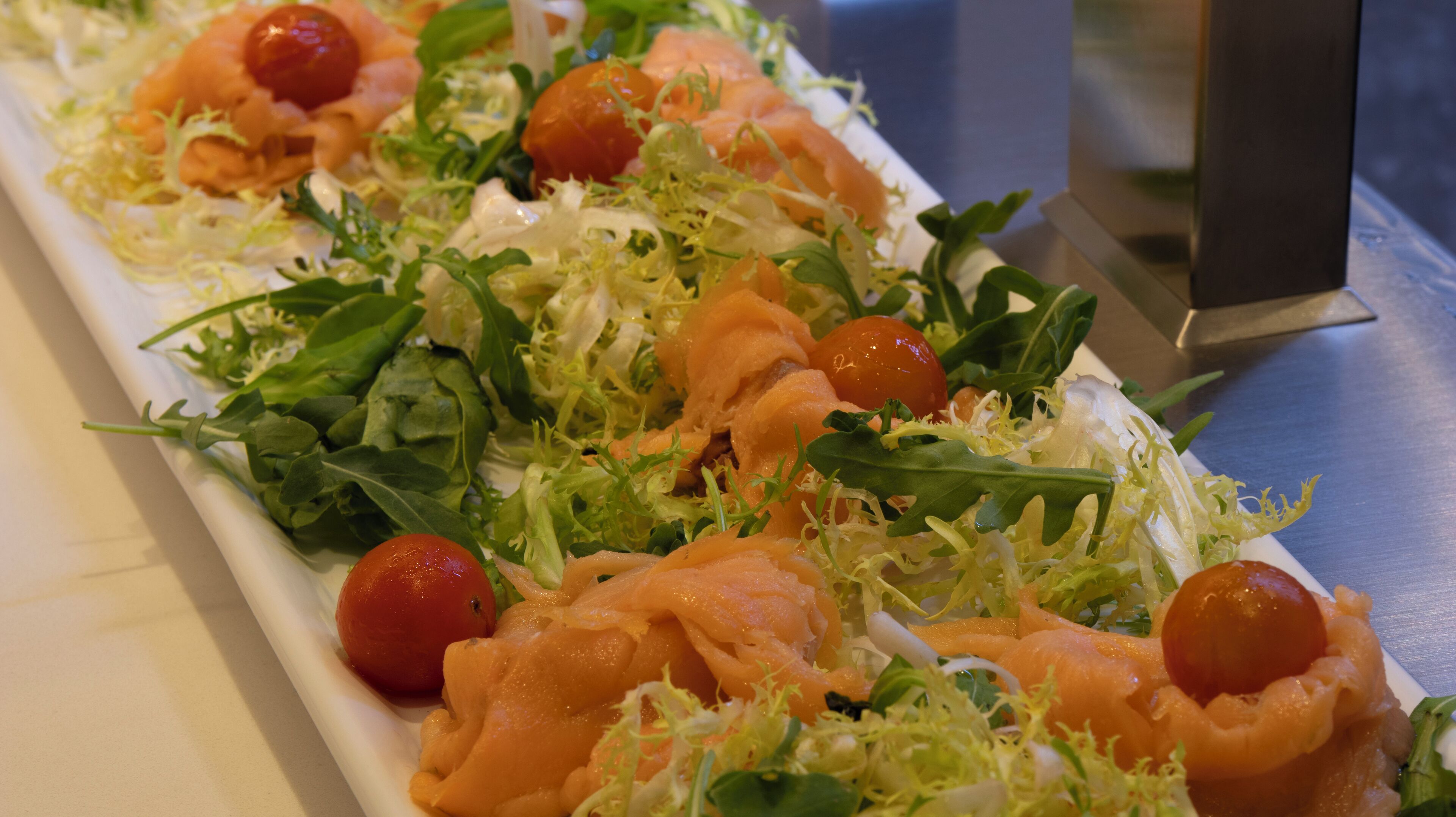 A long rectangular platter with a salad consisting of greens, cherry tomatoes, and salmon slices.