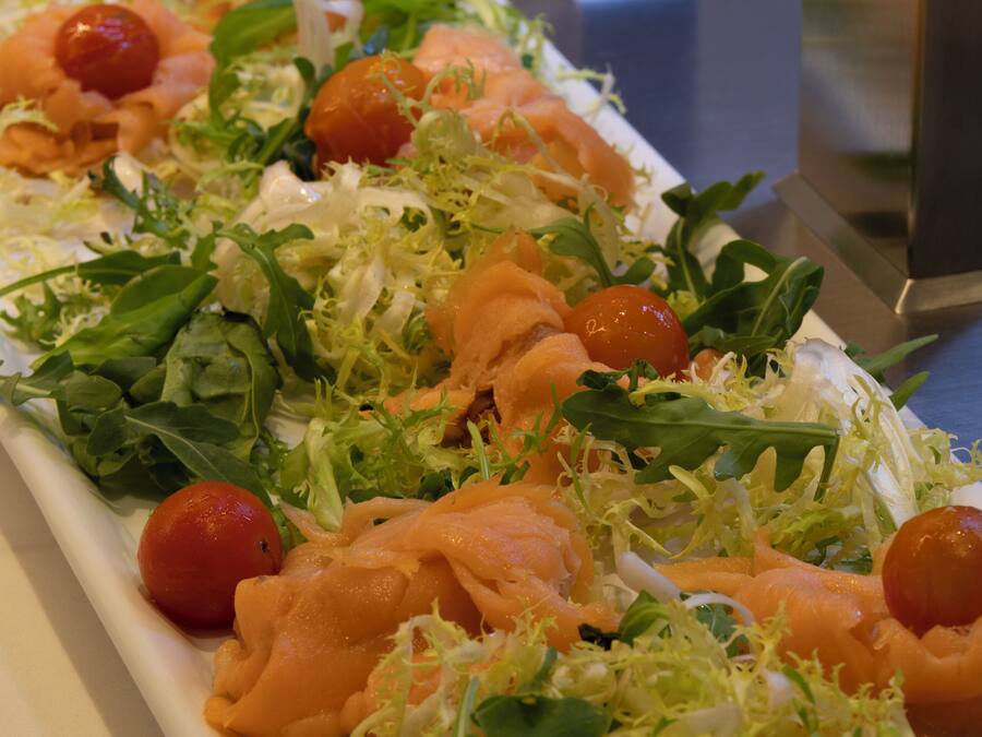 Een lang, rechthoekig schaalplateau met een salade van bladgroenten, kerstomaatjes en stukjes zalm.