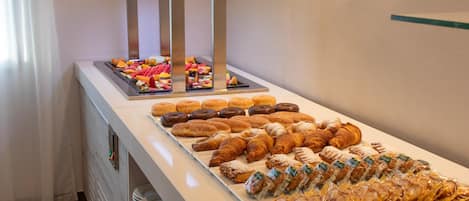 Un bufé con diversas opciones de bollería, como cruasanes y rosquillas, además de una selección de frutas y verduras.