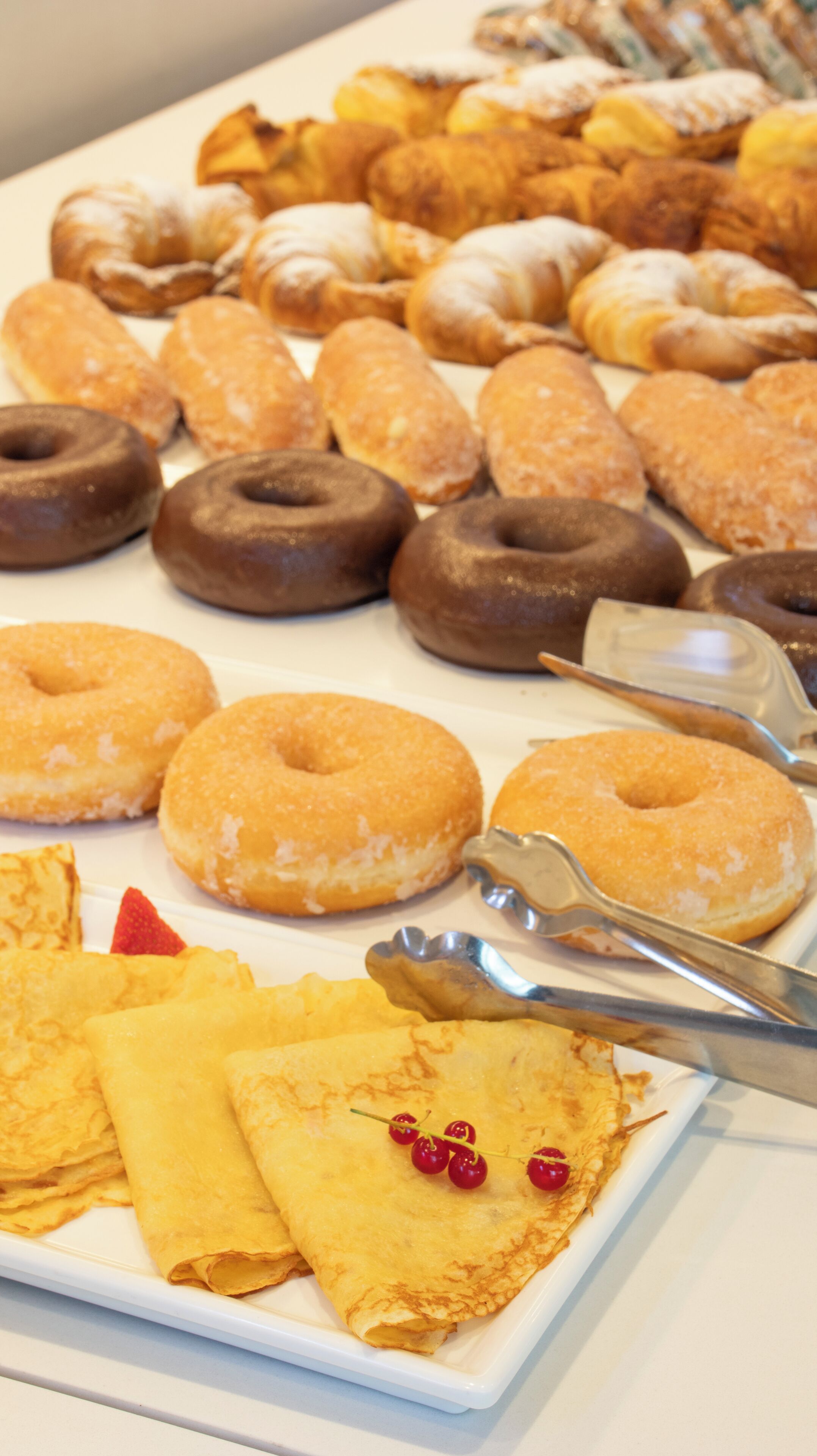 Une variété de pâtisseries et de desserts présentés sur une assiette blanche, notamment des beignets, des croissants et des crêpes.
