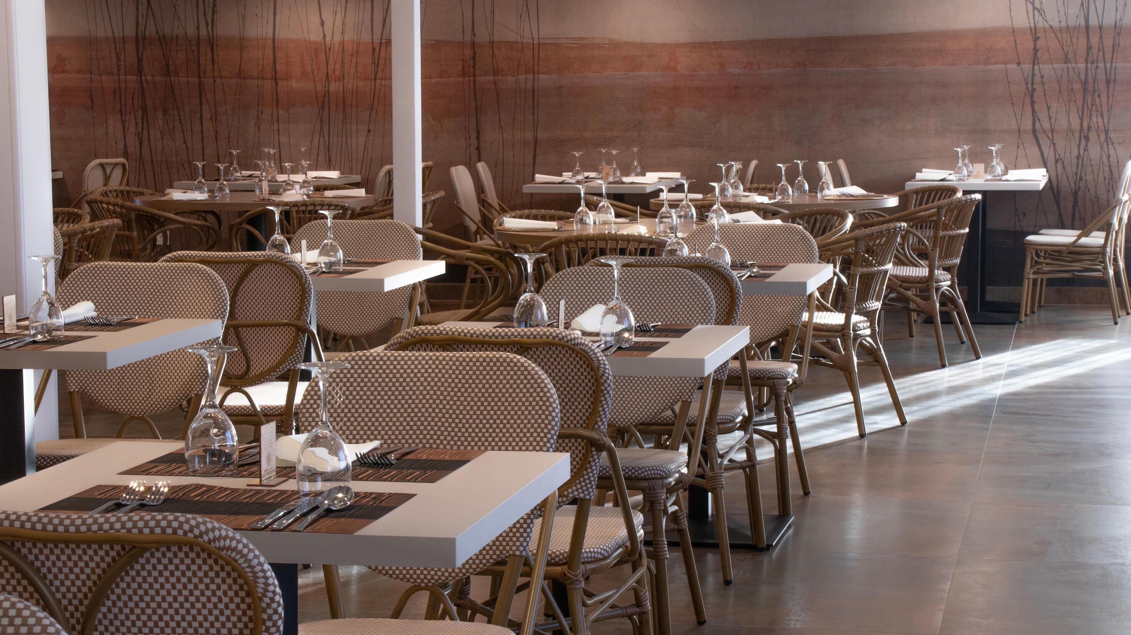 A restaurant with wicker chairs and tables, each set with cutlery, glasses, and a menu.