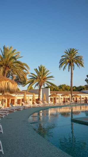 Zona de piscina en un resort con sillas de descanso y palmeras.