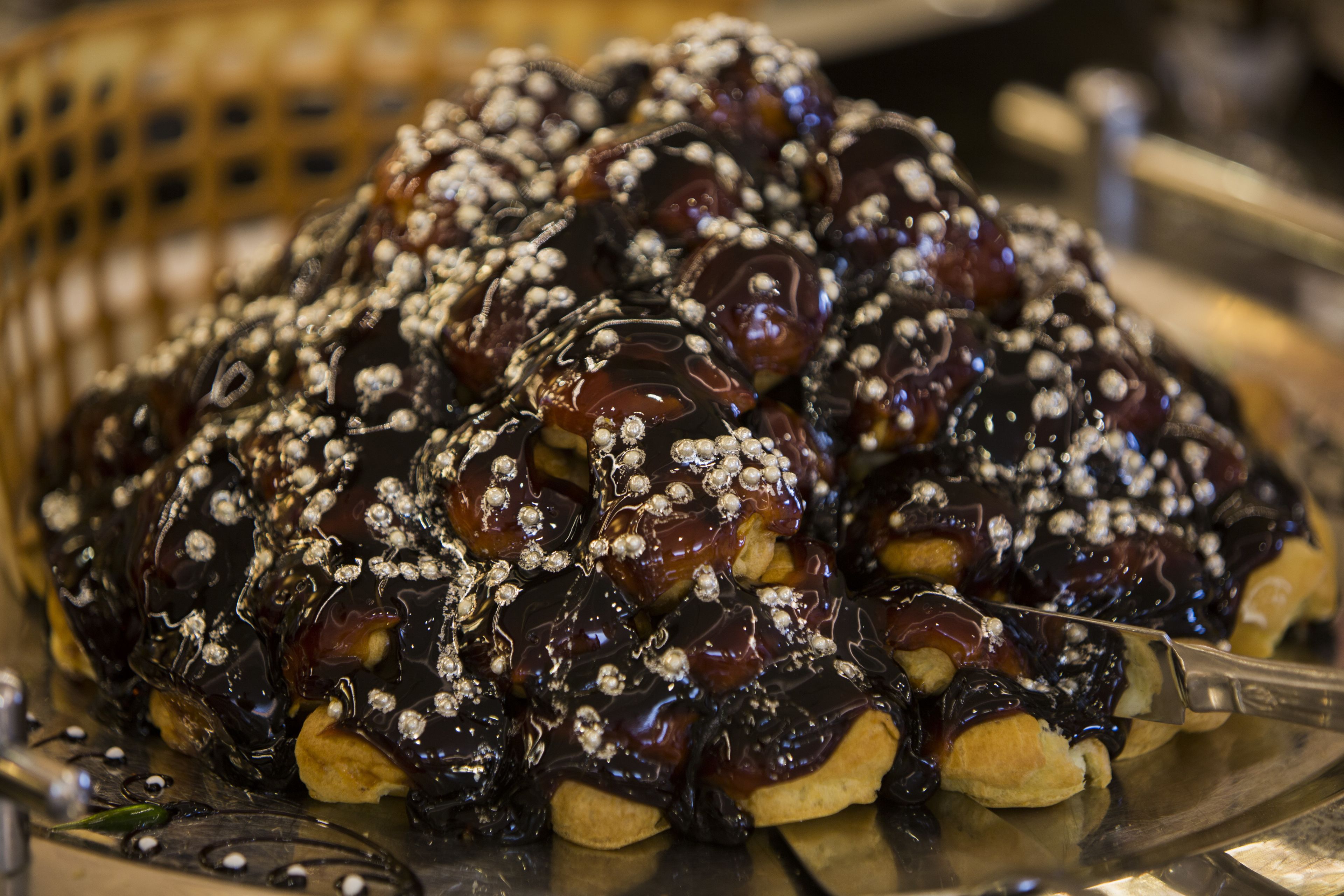A tray of chocolate-covered pastries with a glossy finish and decorative sugar pearls.