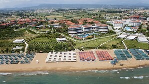 Un resort costero con varias construcciones, una playa con tumbonas y vistas del paisaje circundante.