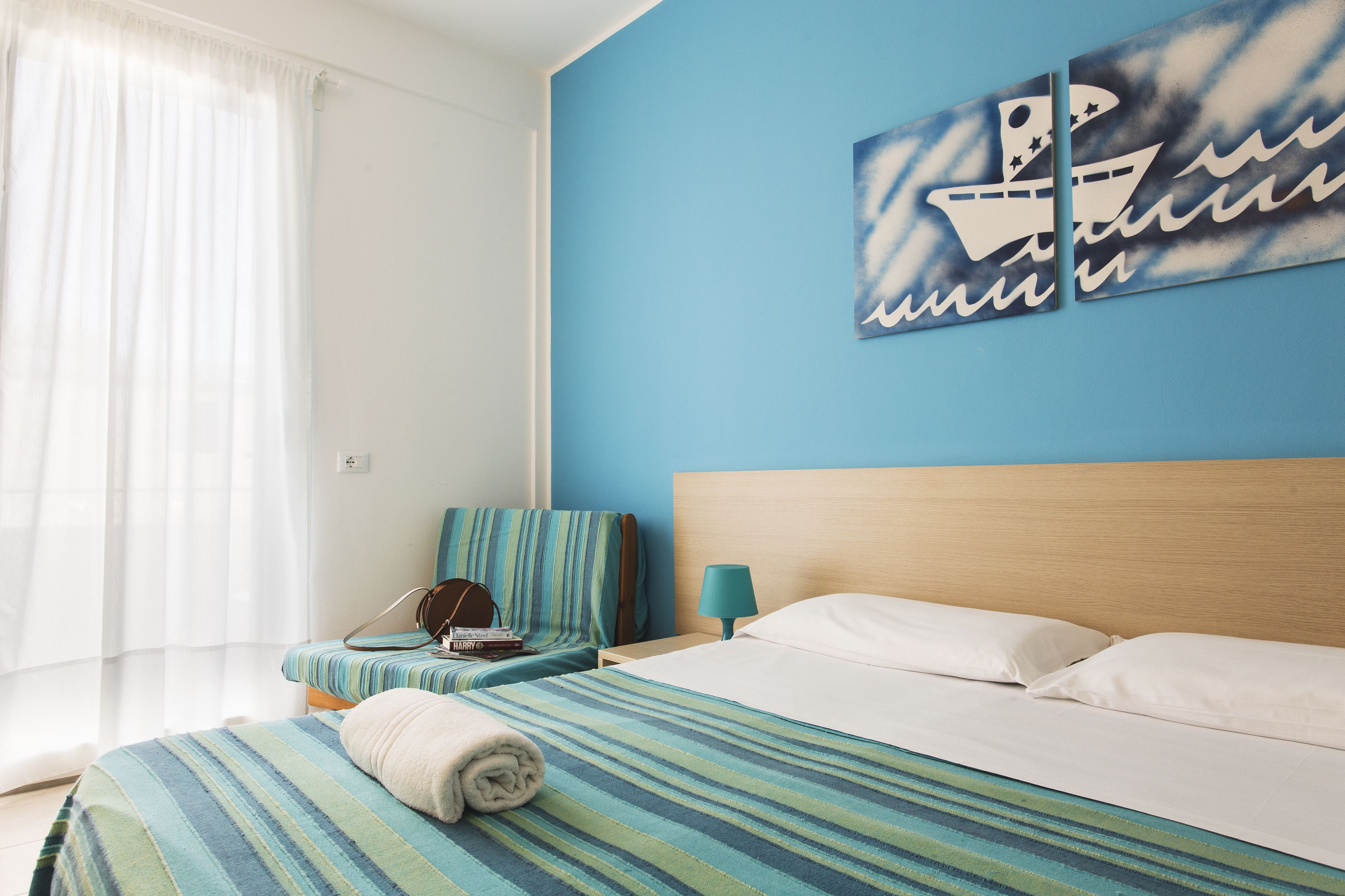 A hotel room with a bed, a bedside table, a chair, and a window with curtains.