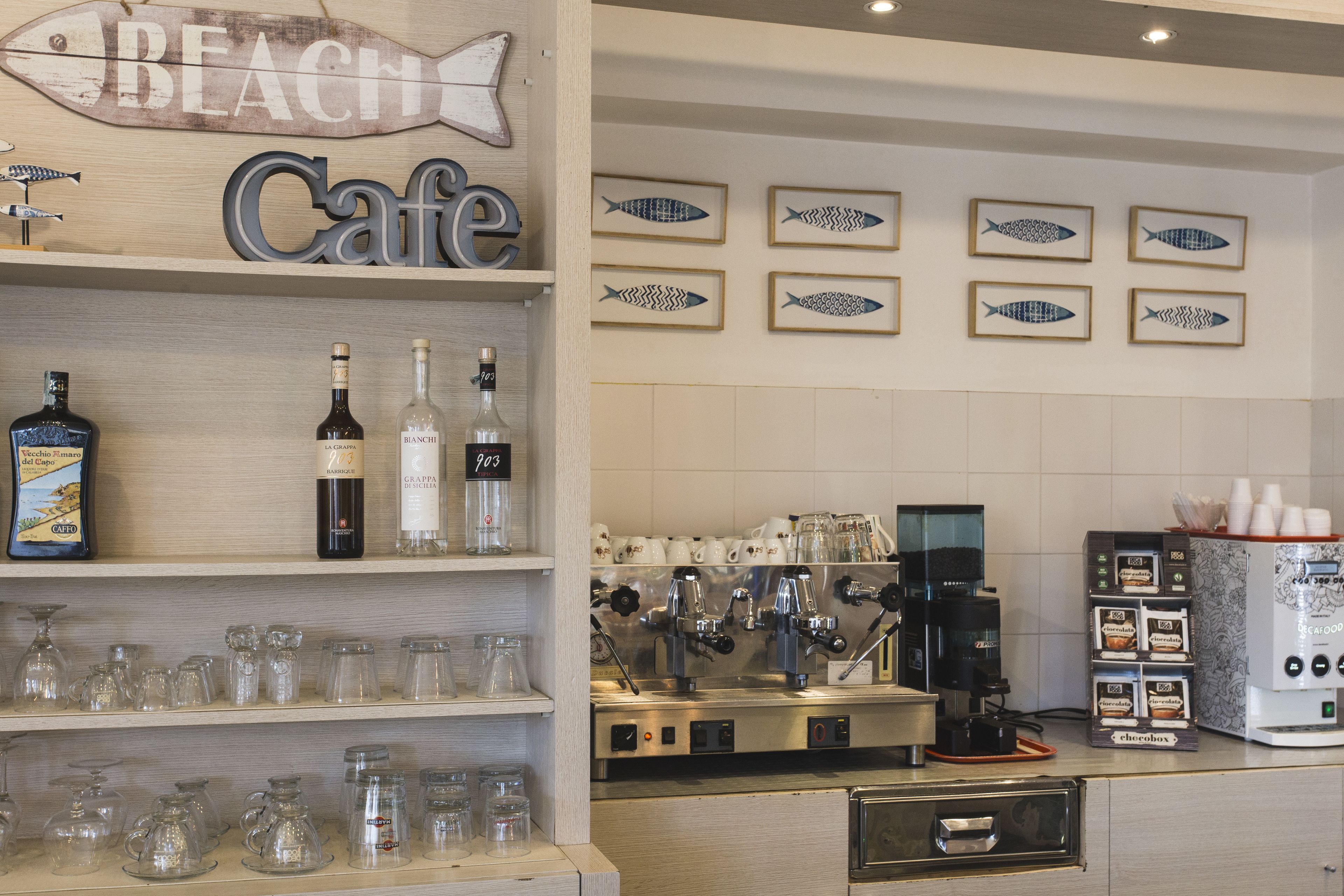 Un café con un letrero de madera que dice "Beach Cafe", máquinas de espresso y varias tazas de café a la vista.