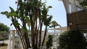 A patio area with a white table and chairs, surrounded by lush tropical plants and a white fence. - Hotel Baia del Sole (Ragusa)