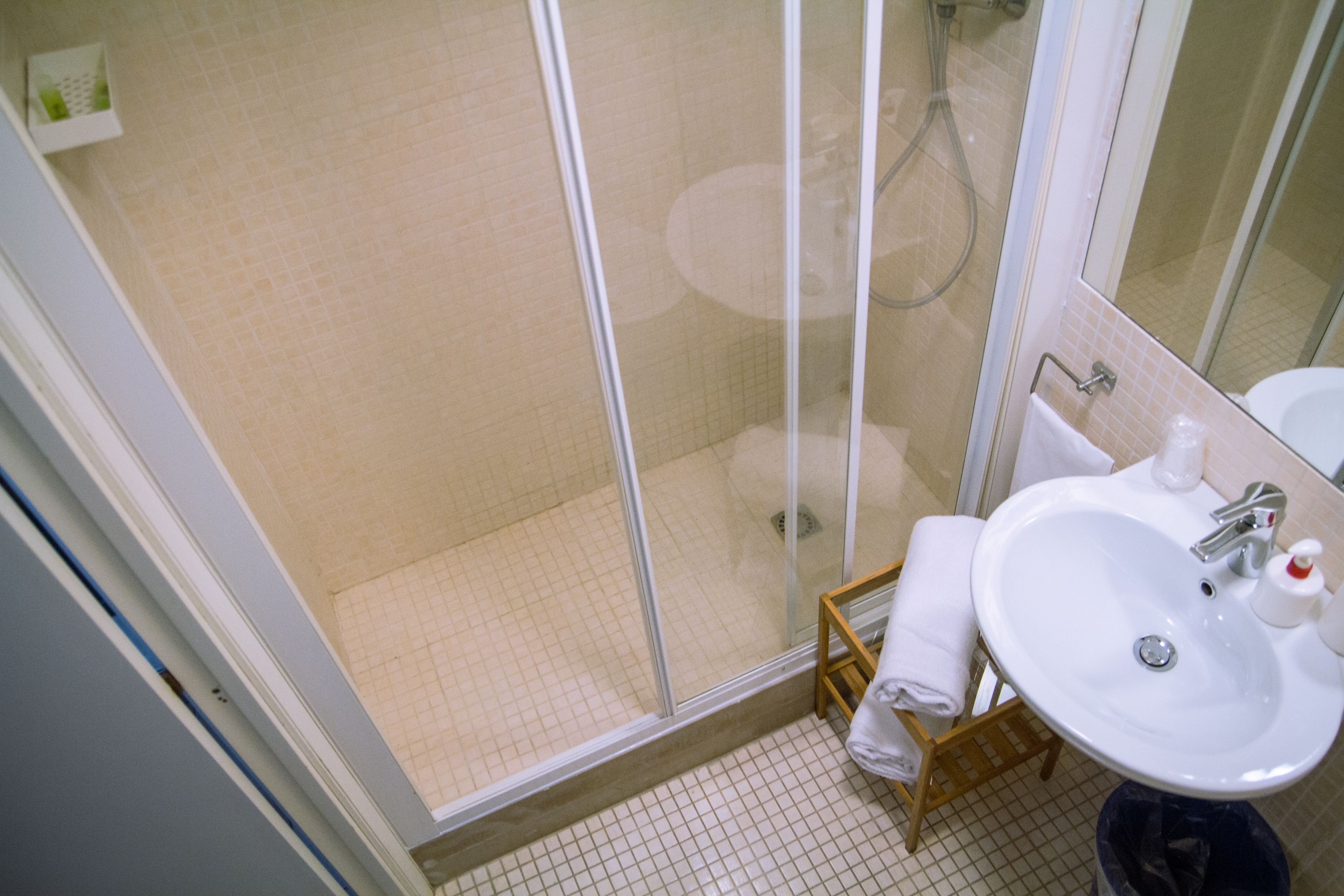 Un baño con ducha de vidrio, lavamanos y un pequeño taburete de madera.