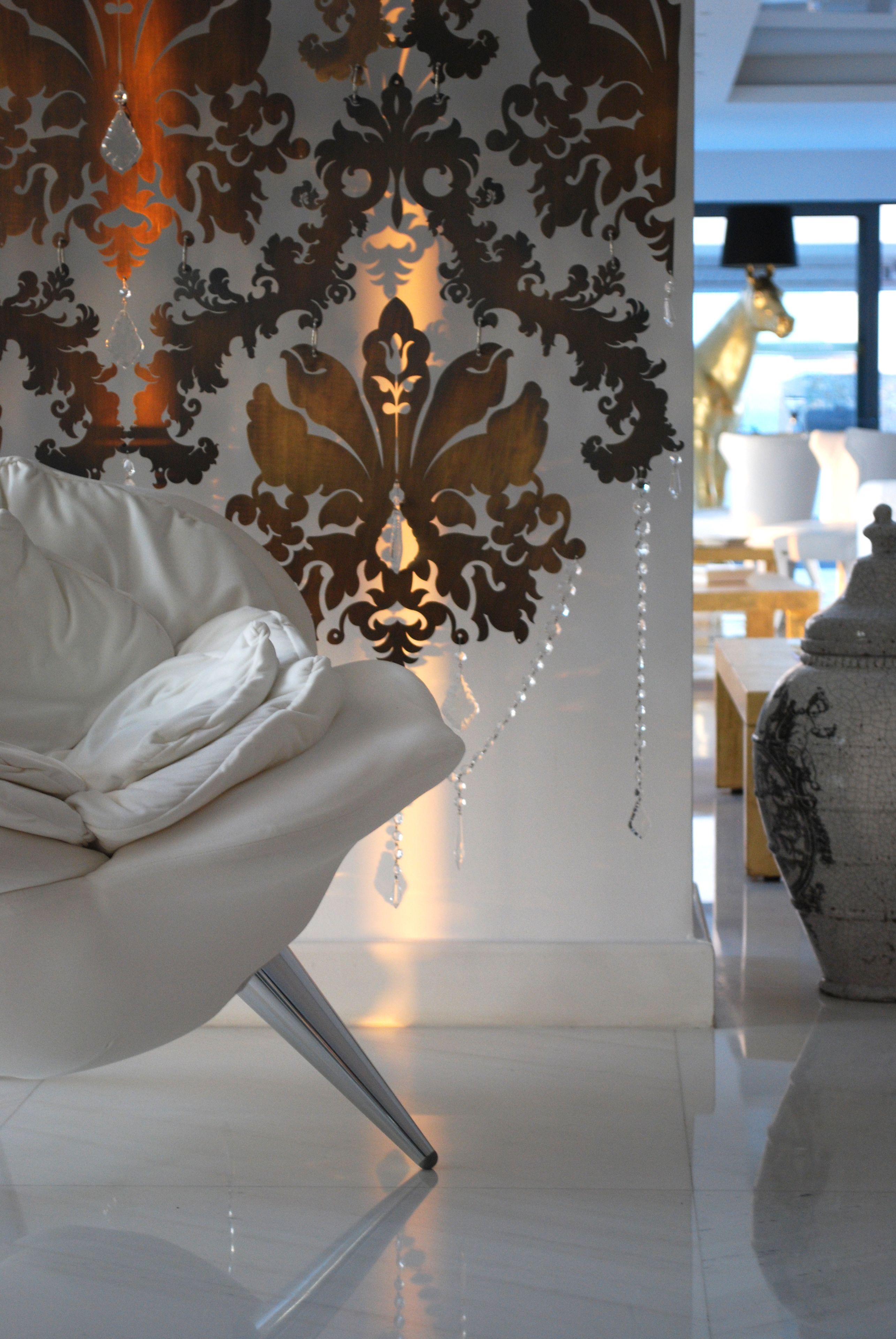 Un interior moderno con un sillón blanco, una pared decorativa con estampado damasco y un jarrón grande.