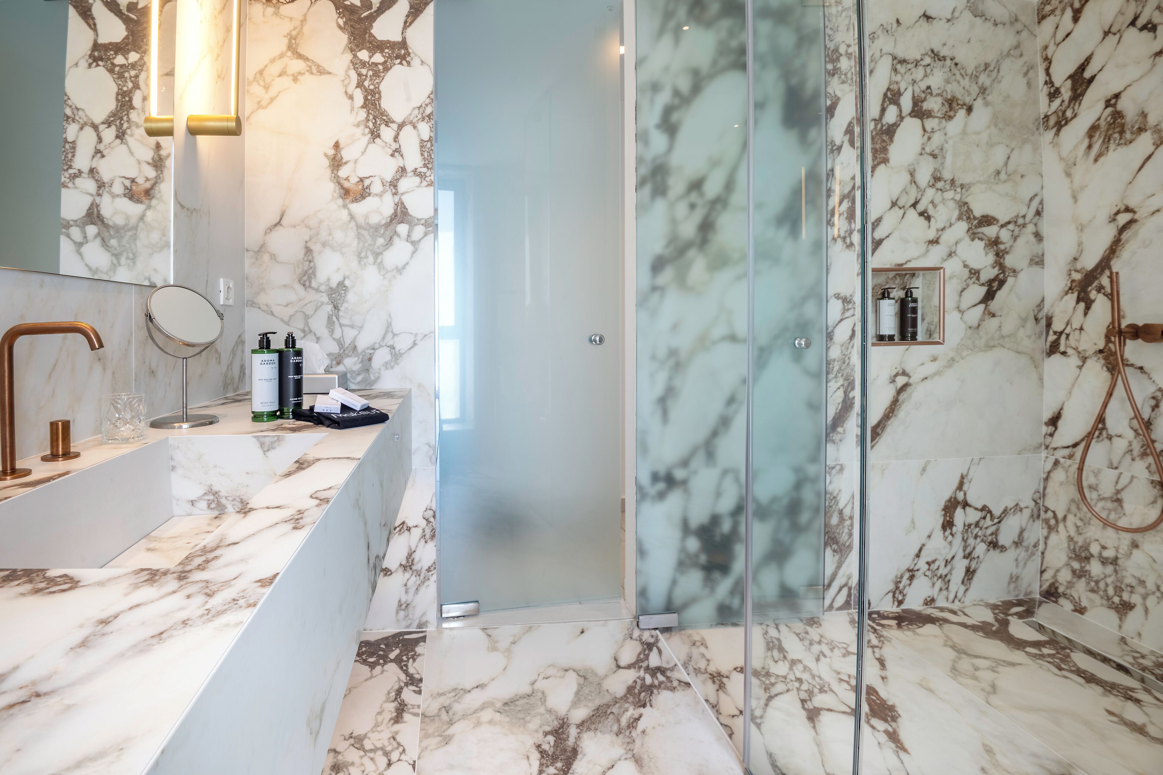 A modern bathroom with a marble vanity, a glass shower enclosure, and a marble-tiled shower area.