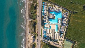Vista aérea de un hotel costero con una amplia piscina, varias habitaciones para huéspedes y una cancha de tenis.