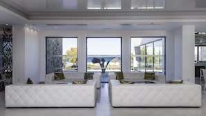 A modern living room with a large sectional sofa, a coffee table, and a view of the sea through large windows.