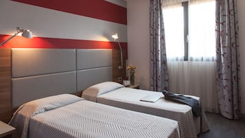 Ett hotellrum med två sängar, ett nattduksbord, en lampa och ett fönster med gardiner.