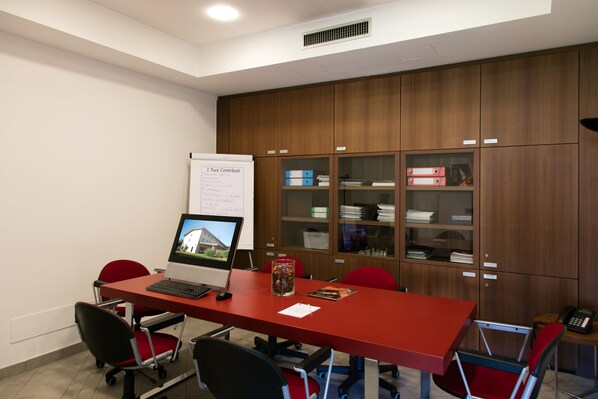 A conference room with a red table, black and red chairs, a whiteboard, and wooden cabinets with glass doors. - Hotel del Parco (Vigevano)