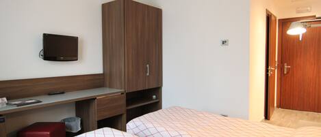 Una habitación de hotel con cama, escritorio, televisor y armario.
