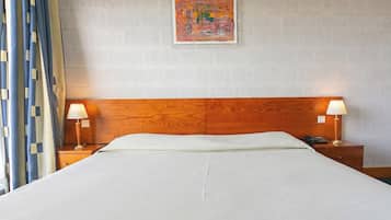 A hotel room with a wooden headboard, two bedside tables with lamps, a bed with white linens, a painting on the wall, and a curtain on the left side.