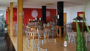 Un'ampia sala da pranzo con diversi tavoli e sedie rotondi, una parete d'accento rossa e un pilastro nero.