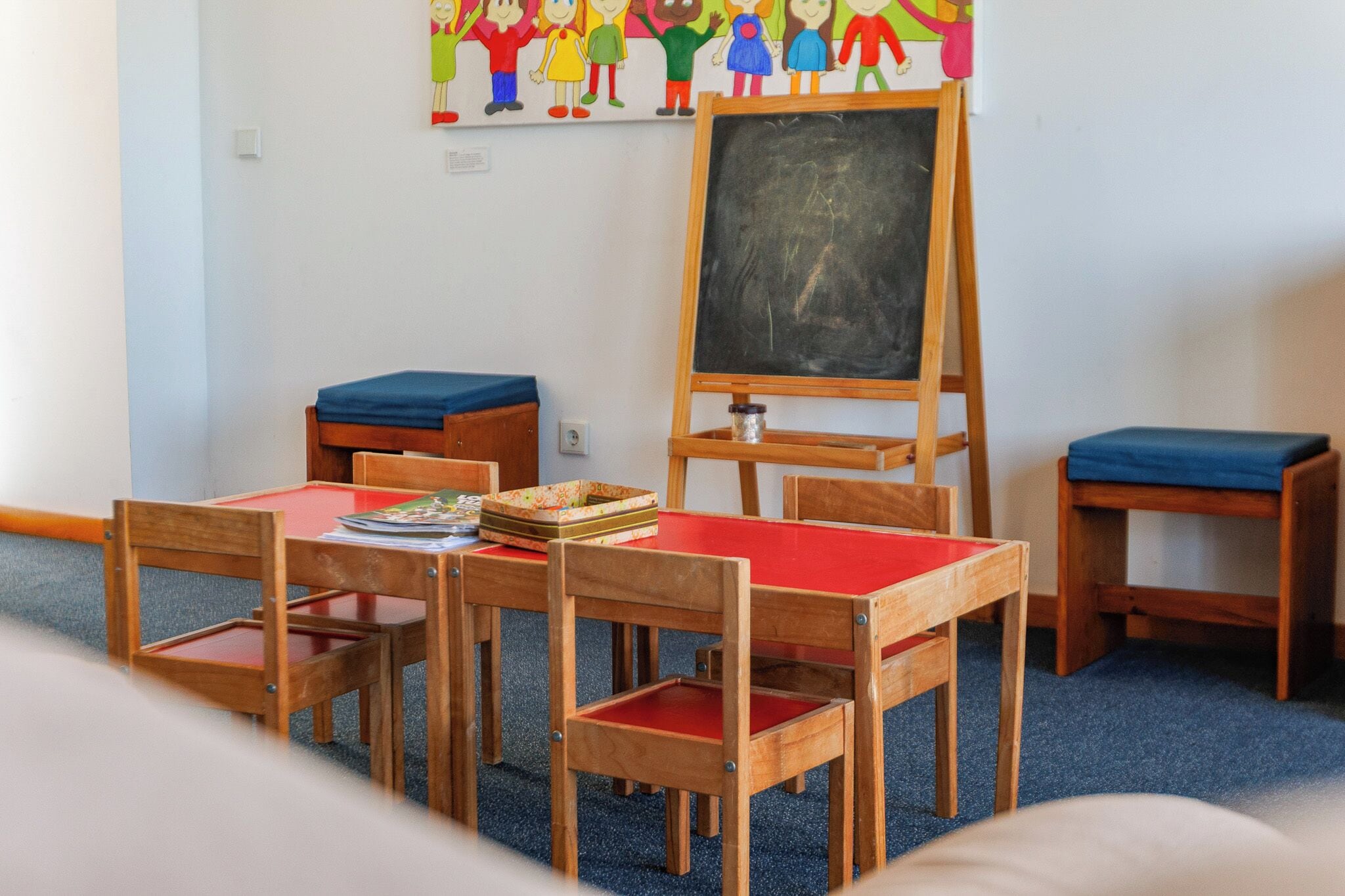 A classroom with wooden furniture, a chalkboard, and a children's artwork on the wall.