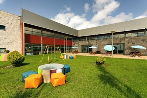 A courtyard with a swing set, outdoor seating, and a building with large windows. - Hotel Colombo (Vila do Porto)