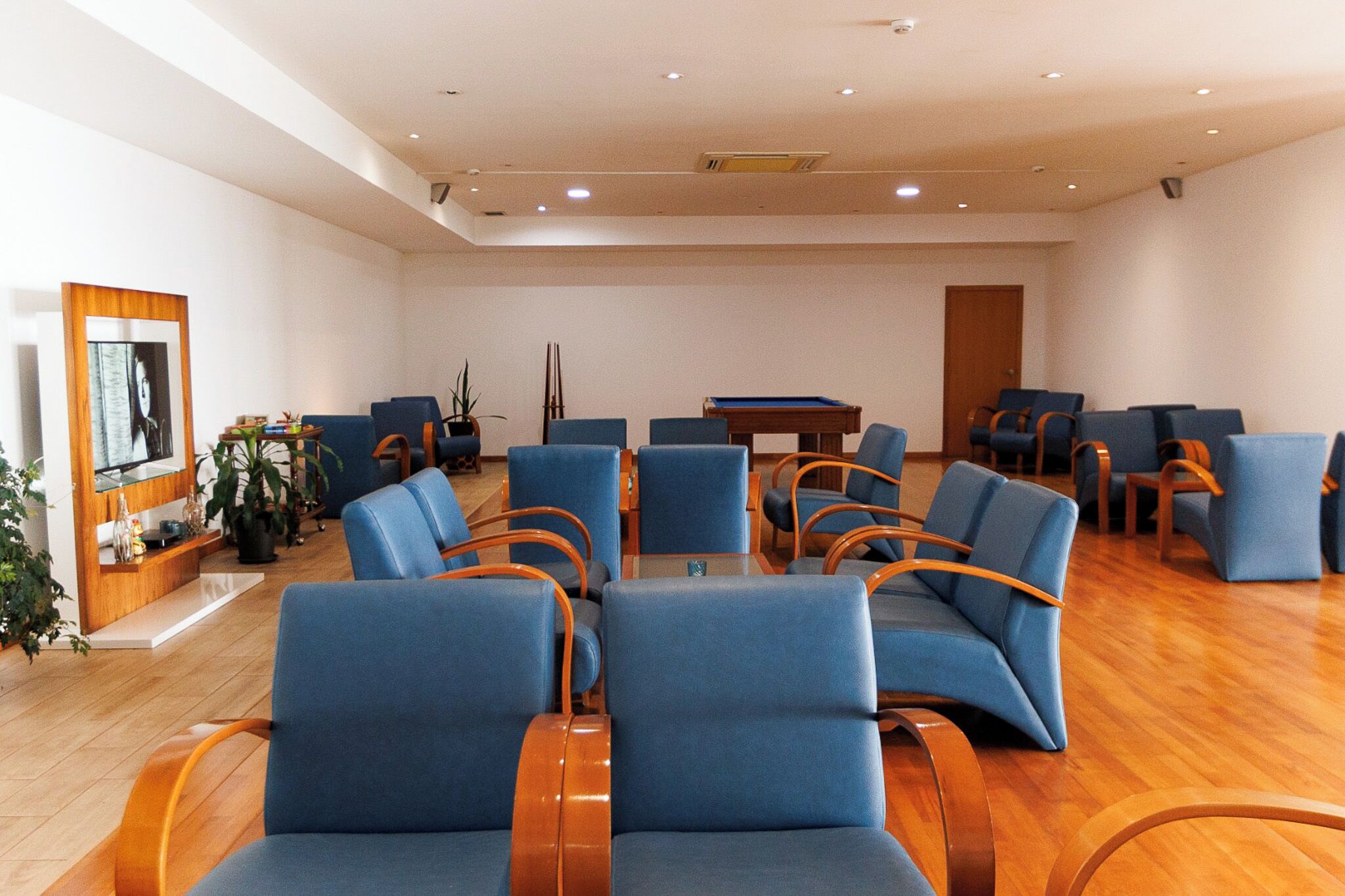 A room with blue chairs arranged around a pool table, wooden flooring, and a door in the background.