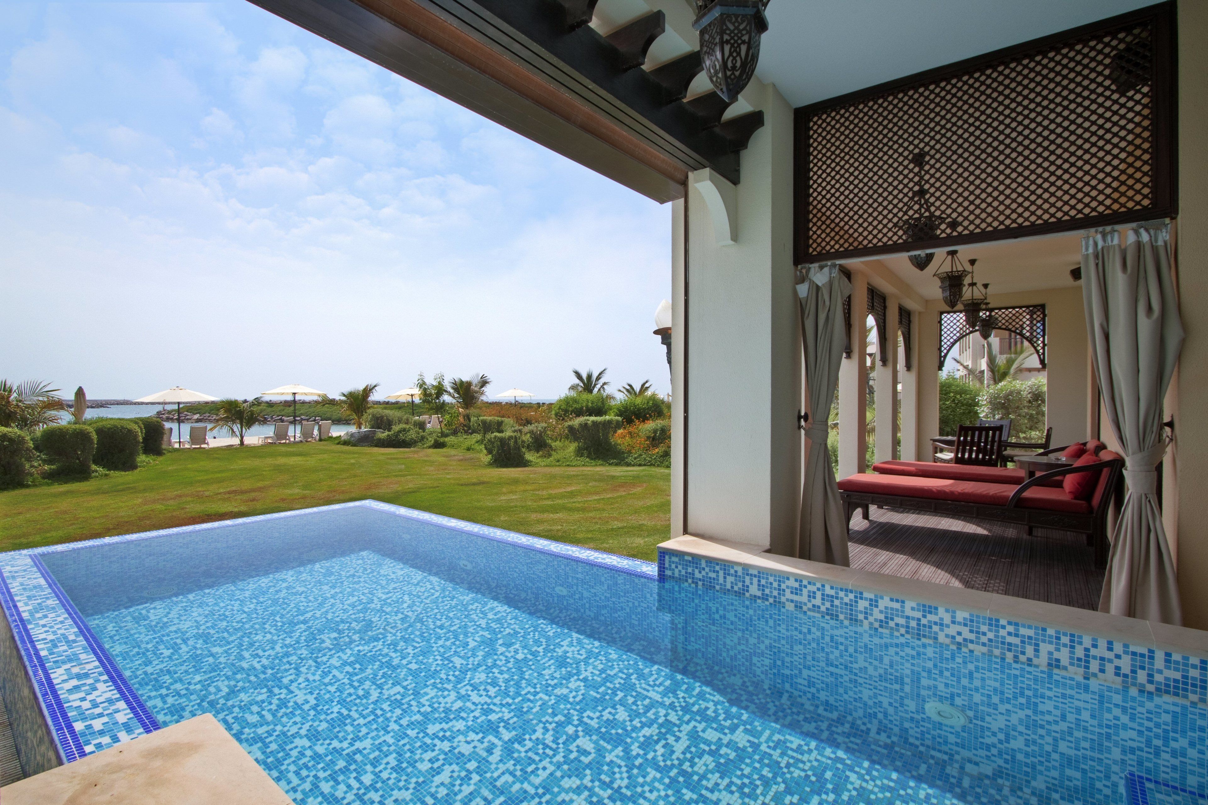 Una piscina con vista al mar, una silla de descanso roja y una zona de estar exterior cubierta.