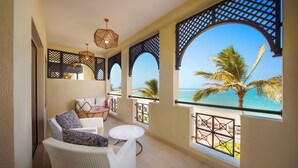 A balcony with white wicker furniture, a small round table, and a view of the beach and palm trees. - Rixos Al Mairid Ras Al Khaimah (Ras Al Khaimah)