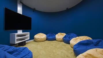 A room with a flat-screen TV mounted on a white stand, surrounded by blue and beige bean bag chairs on a beige carpet.