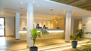 Et moderne receptionområde med en træreception, to receptionistmedarbejdere og plantekasser.