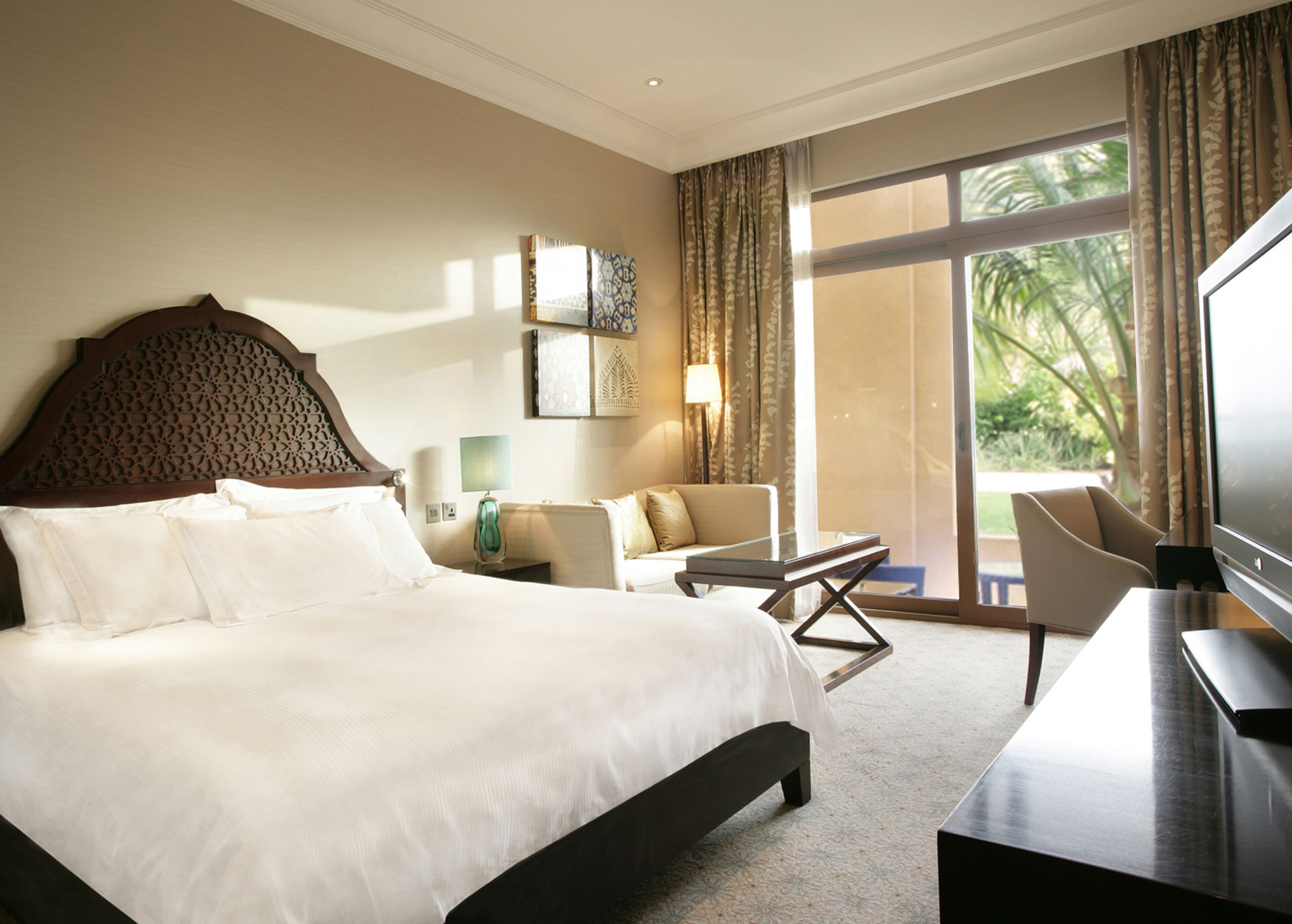 A hotel room with a large bed, a desk, a chair, a TV, and a view of the outdoors.