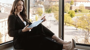 Une personne assise près d’une grande fenêtre, d’où l’on peut admirer le paysage urbain.