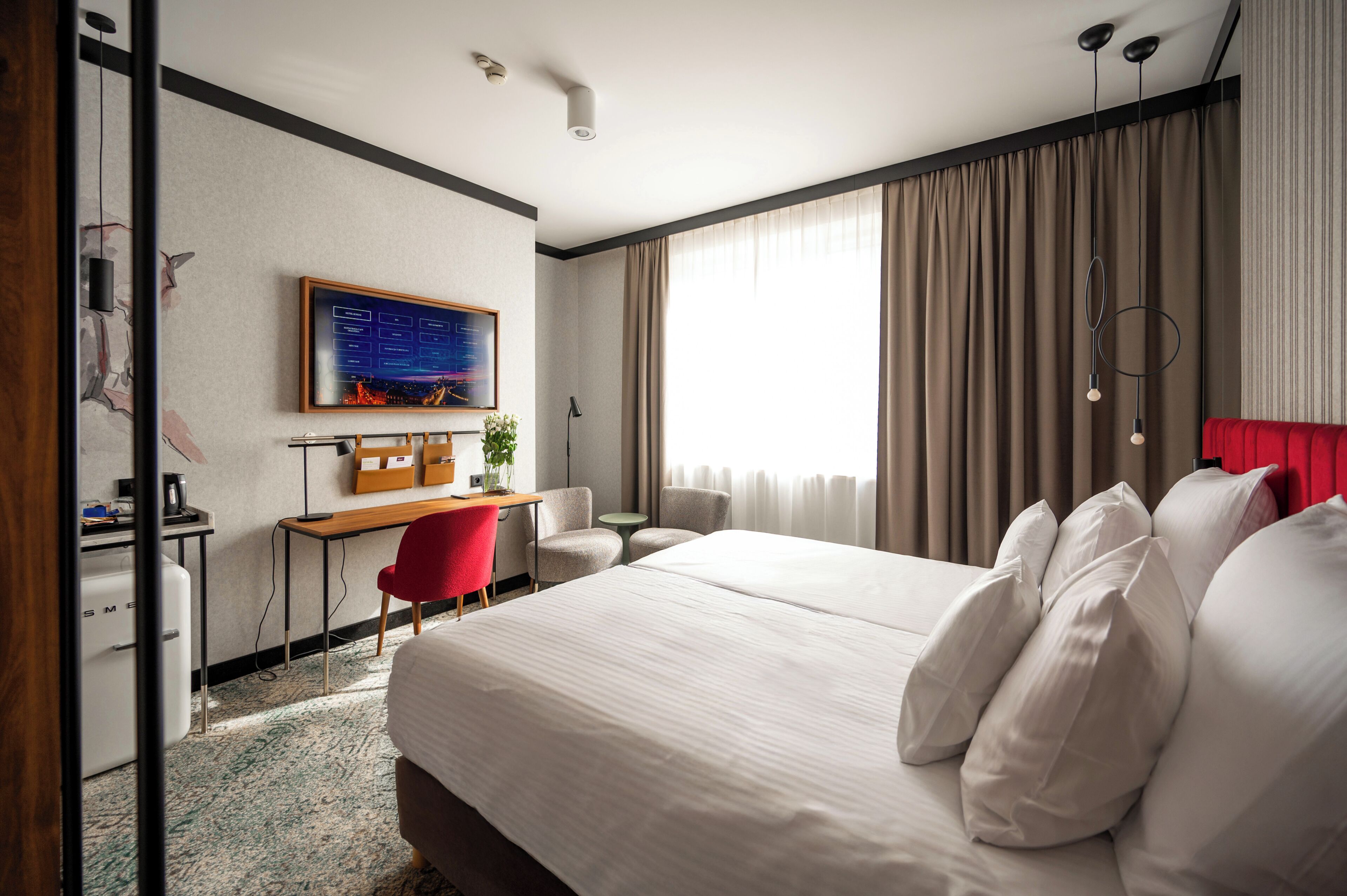 Habitación de hotel con una cama grande, un escritorio, una silla, un televisor y una ventana con cortinas.