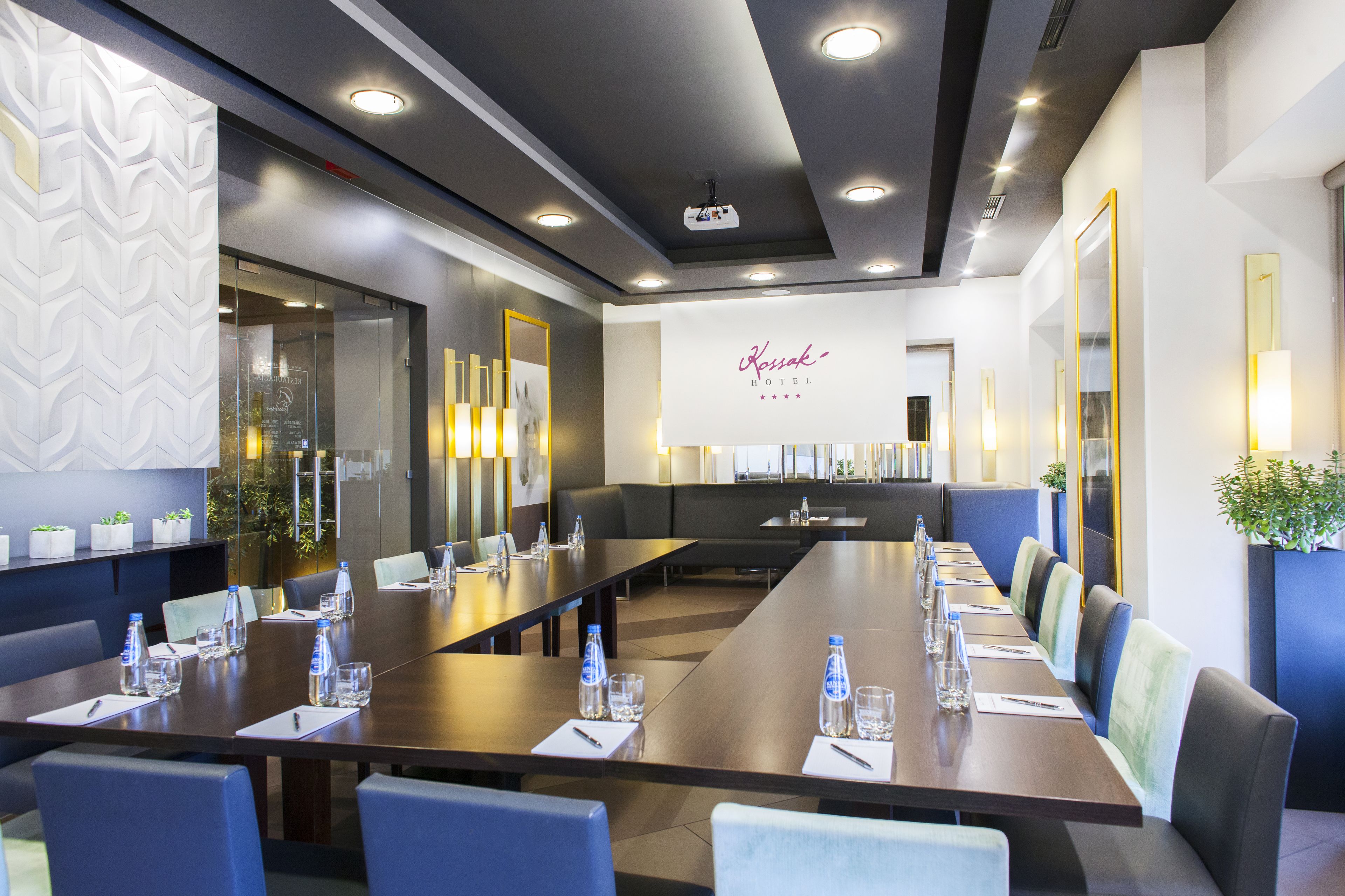 Une salle de conférence avec une longue table, des chaises, des bouteilles d’eau et un panneau indiquant l’hôtel Kessak.