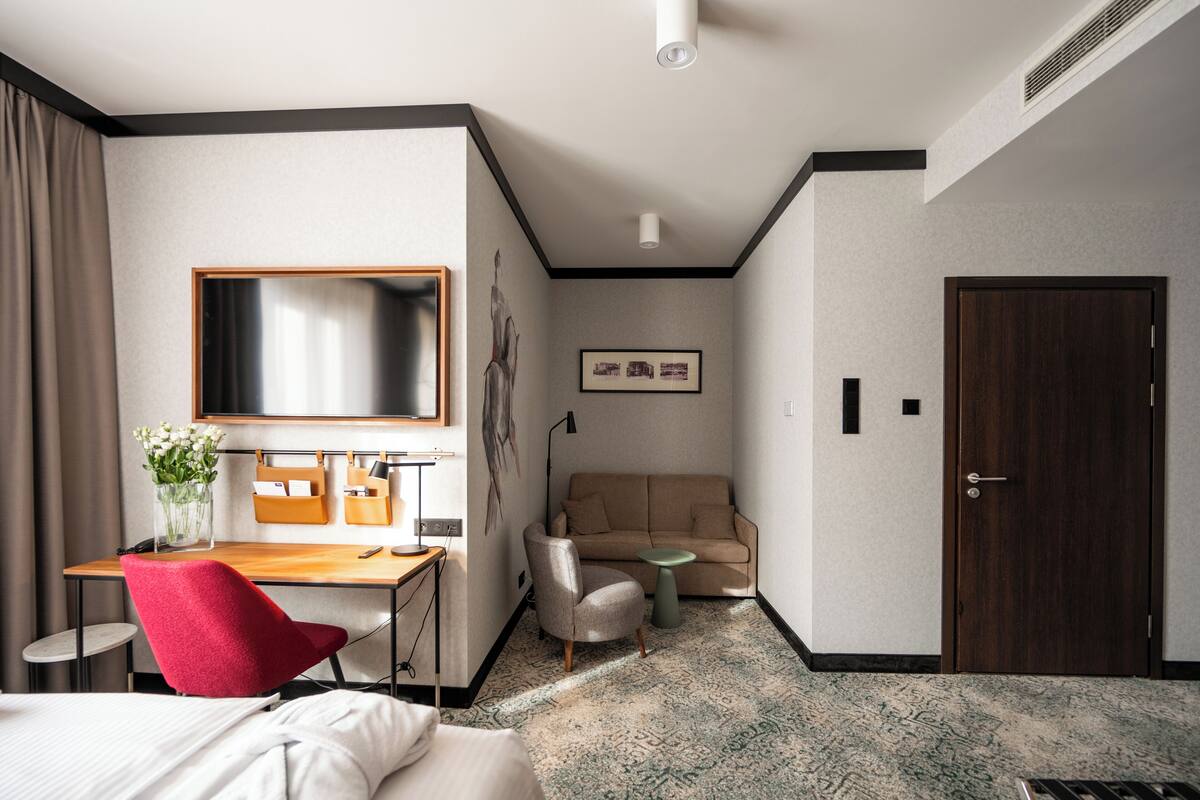 A hotel room with a bed, a desk with a chair, a sofa, a small table, a TV, and a door.