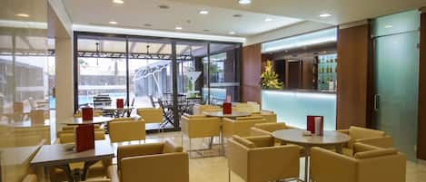 A modern indoor seating area with tables and chairs, a bar area with a counter, and a view of an outdoor pool.