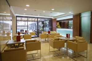 A modern indoor seating area with tables and chairs, a bar area with a counter, and a view of an outdoor pool. - Antillia Hotel (Ponta Delgada)