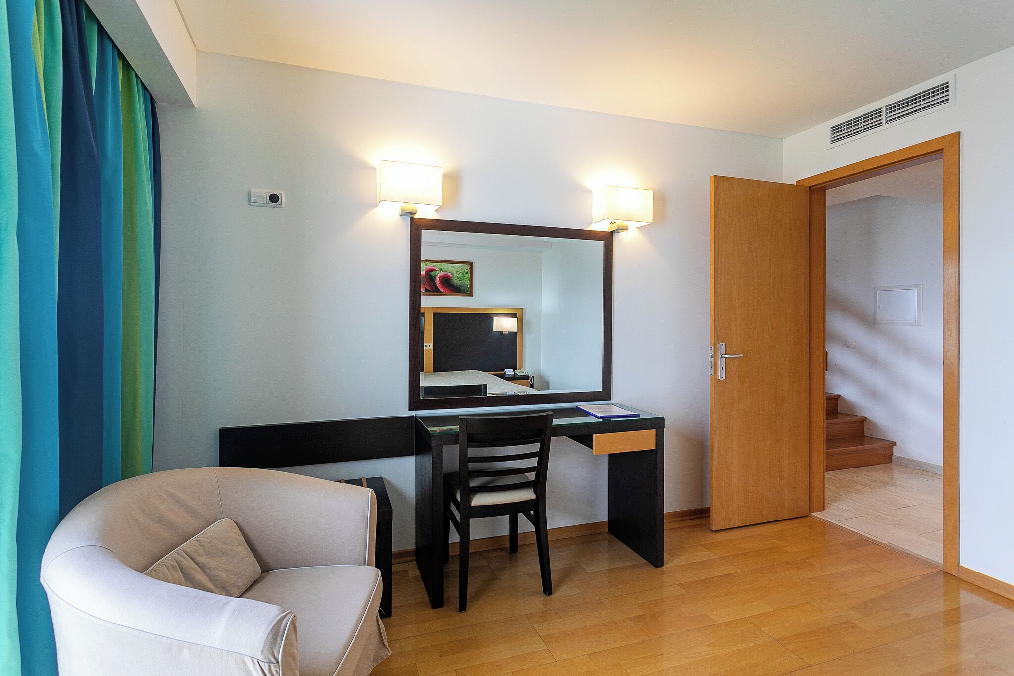 Habitación de hotel con escritorio, silla y cama. Se observa una puerta que da a una escalera.