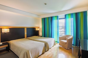 A hotel room with two beds, a chair, and a view of the city through large windows.
