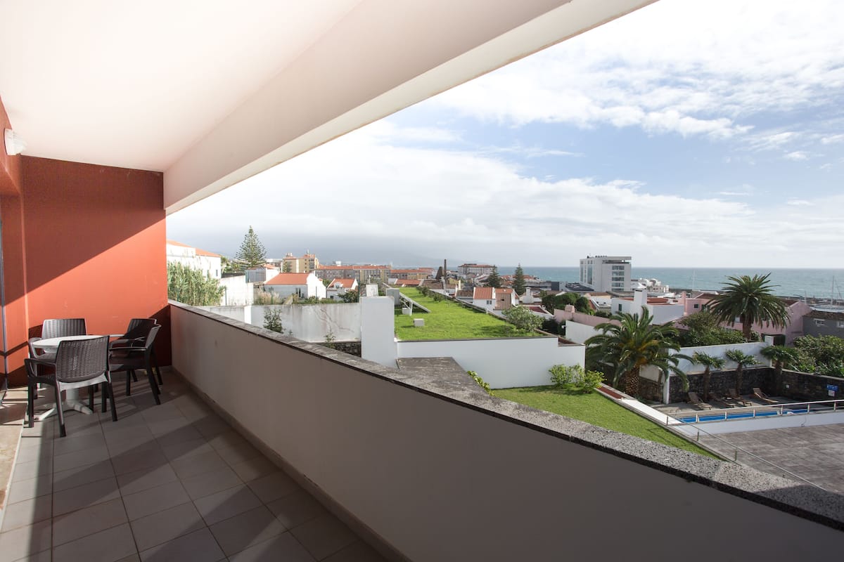 A balcony with a view of a residential area, a swimming pool, and the sea.
