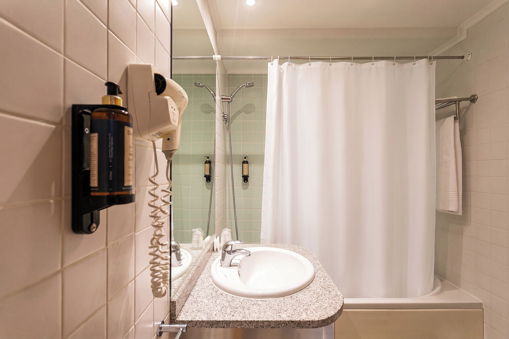 Ein Badezimmer mit Waschbecken, Föhn, Dusche und Handtuchhalter.