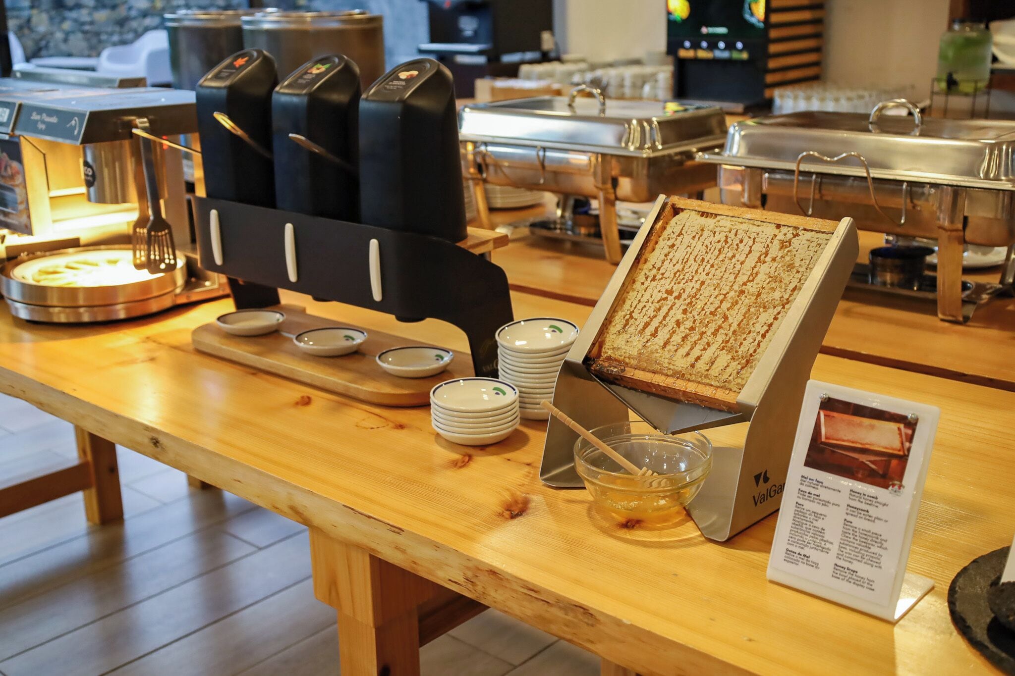 A buffet setup with various food stations, including a griddle, a honey dipper, and a sign with menu items.