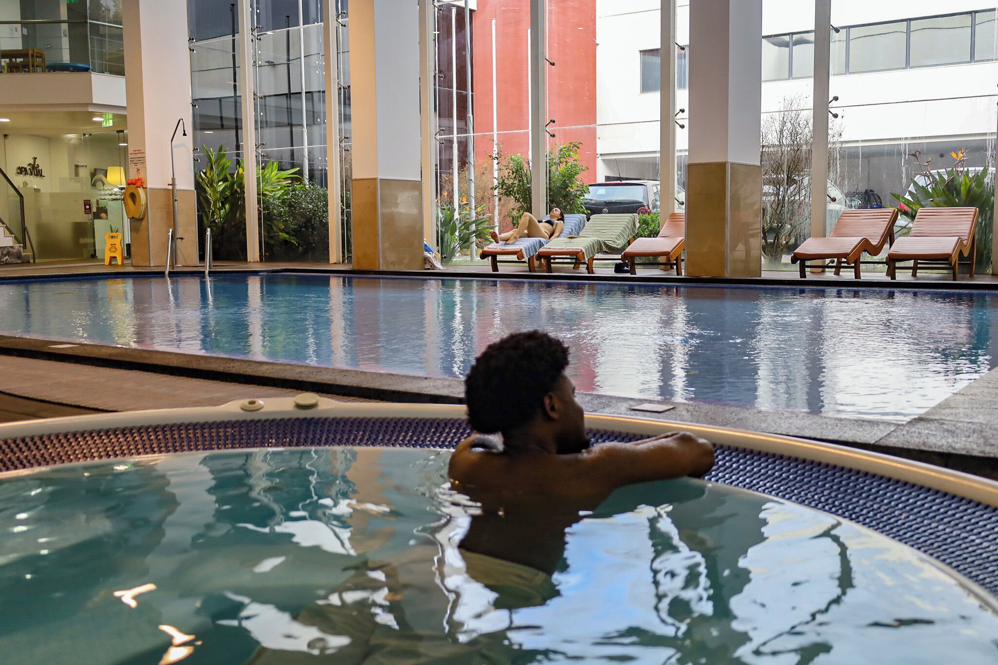 An indoor swimming pool with lounge chairs and a person relaxing in the water.